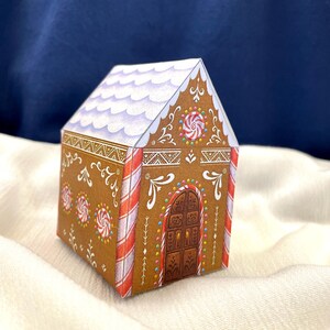 May include: A paper gingerbread house with brown walls, white frosting, and red and white candy cane stripes. The roof is white with purple accents. The house is decorated with candy and swirls.