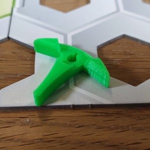 Puede incluir: Una pieza de juego de pl&aacute;stico verde brillante con forma de gancho. La pieza tiene un peque&ntilde;o agujero en el centro.