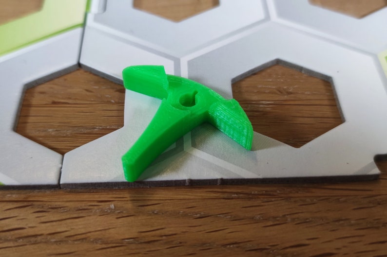 Puede incluir: Una pieza de juego de pl&aacute;stico verde brillante con forma de gancho. La pieza tiene un peque&ntilde;o agujero en el centro.