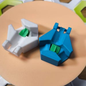 May include: Two 3D printed keycaps, one white and one blue, with a green accent piece in the center of each. The keycaps are designed to fit on mechanical keyboards.