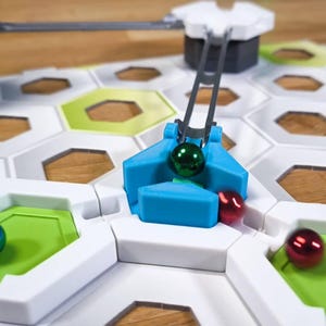 May include: A blue and white marble run game with a green, red, and blue marble. The blue marble is being lifted by a lever.