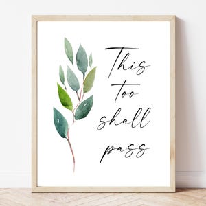 May include: A framed print with a watercolor illustration of a green leafy branch and the text "This too shall pass".