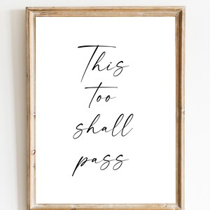 Könnte beinhalten: Ein gerahmter Druck mit dem Text "This too shall pass" in schwarzer Kursivschrift auf weißem Hintergrund.