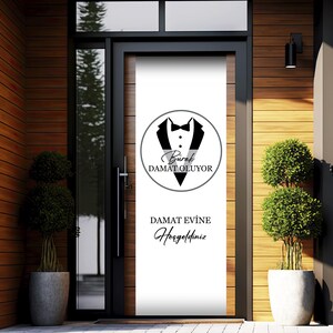 May include: A white door with a black and white sign that says "Burak DAMAT OLUYOR" and "DAMAT EVINE Hosgeldiniz". The sign features a tuxedo with a bow tie.
