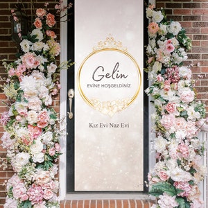 May include: A white door with a gold-framed sign that reads "Gelin Evine Hosgeldiniz" and "Kiz Evi Naz Evi". The door is decorated with pink and white flowers.
