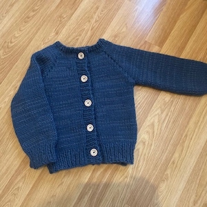 May include: A blue knitted cardigan with a button fastening. The cardigan has a ribbed texture and is made of a soft, comfortable material.