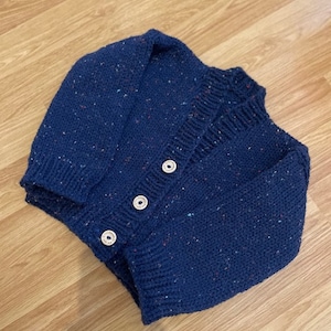 Op de afbeelding: Een donkerblauwe gebreide cardigan met een gespikkelde textuur en drie witte knopen.