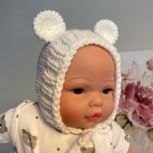 May include: White knitted baby hat with bear ears. The hat has a tie that can be tied under the chin.