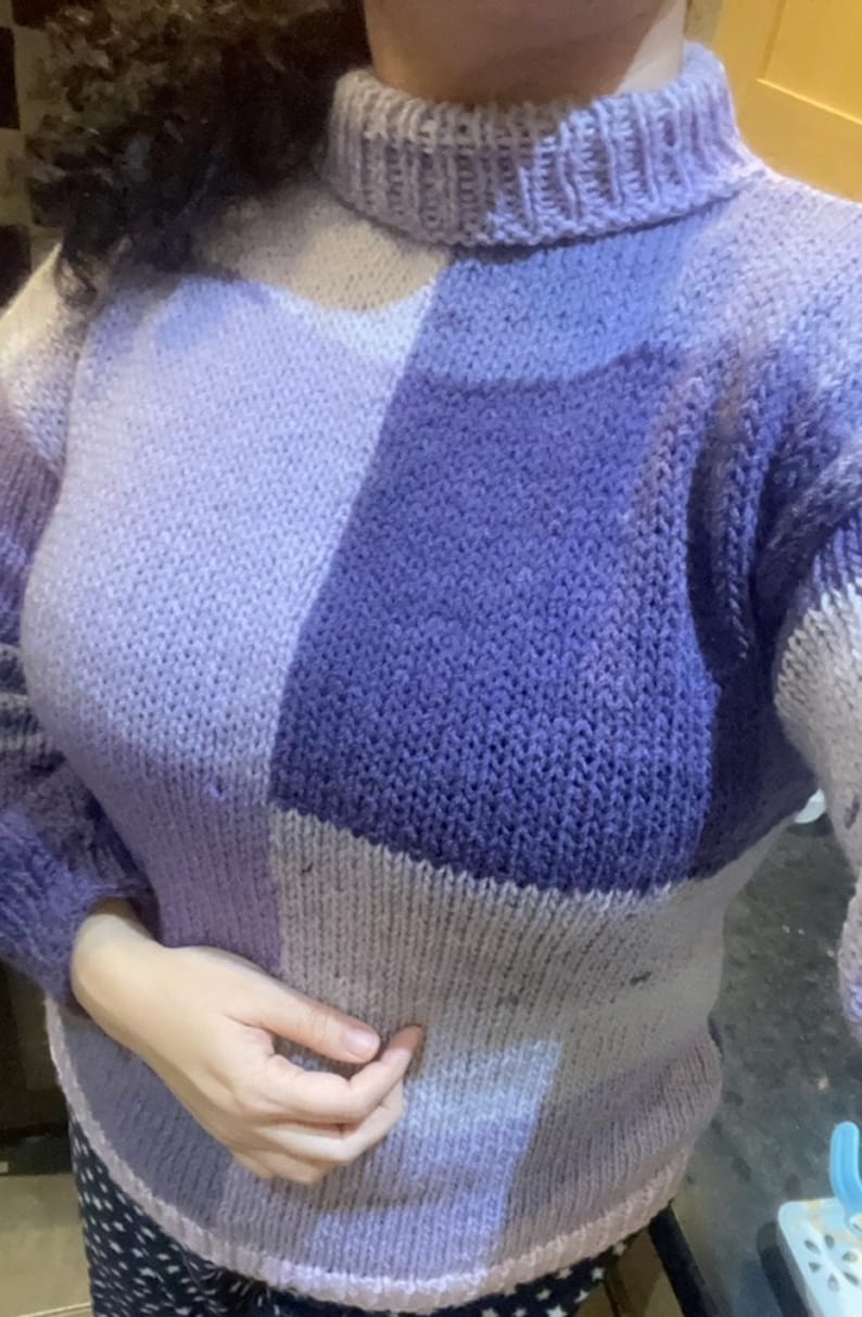 May include: A purple and lavender knitted sweater with a high neck and a patchwork design.