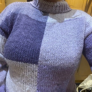 May include: A purple and white knitted sweater with a high neck and long sleeves.