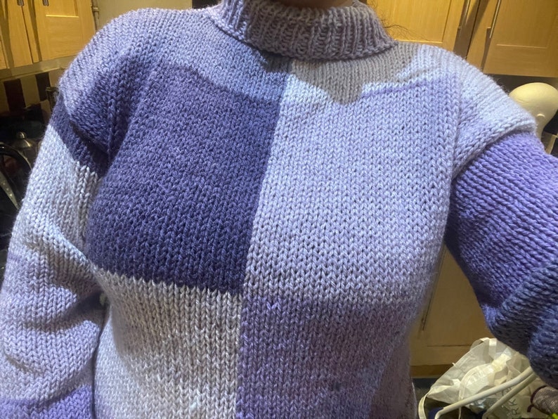 May include: A purple and white knitted sweater with a high neck and long sleeves.