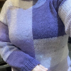 May include: A purple and pink knitted sweater with a high neck and a checkered pattern.