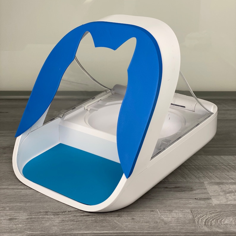 May include: White and blue automatic pet feeder with a clear plastic lid and a blue cat-shaped cutout. The feeder has a blue mat on the bottom.