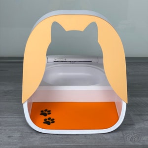 May include: A white and yellow cat litter box with a removable top and a orange mat with paw prints. The litter box has a built-in scoop and a cat-shaped cutout in the top.