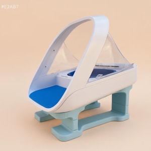 Puede incluir: Un moderno transportín para mascotas en blanco y azul. El transportín tiene una parte superior transparente y arqueada y un asa. La base es azul claro y el interior presenta una almohadilla azul. El diseño es elegante y futurista.