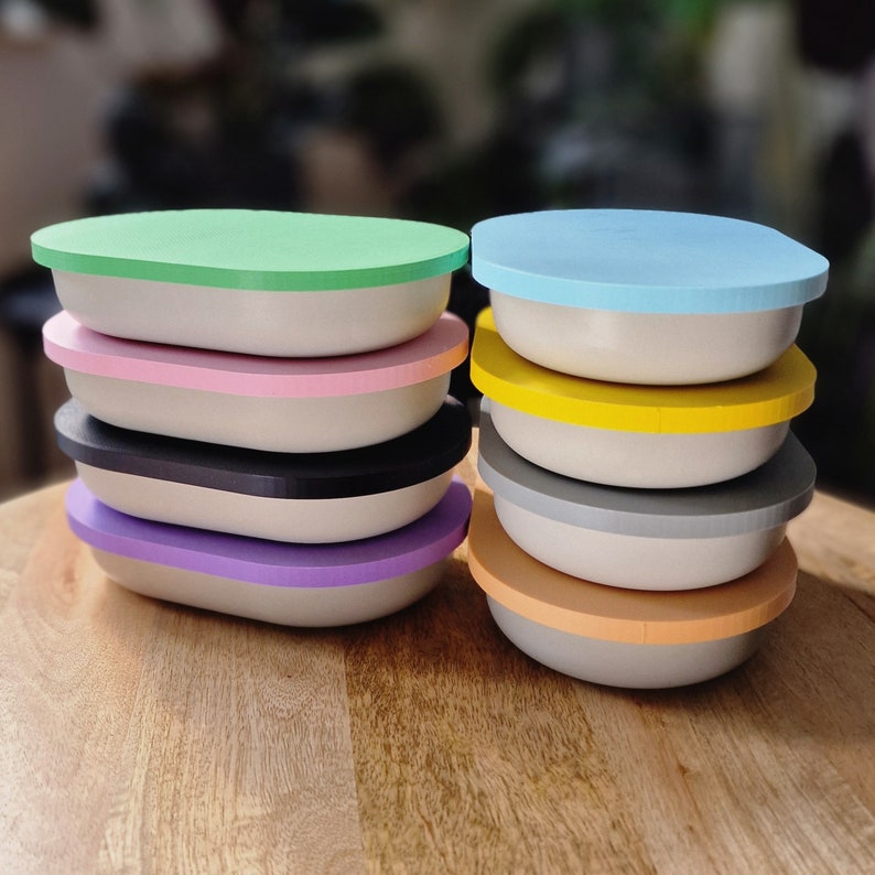 May include: A stack of ten oval-shaped containers with colorful lids. The lids are in the following order from top to bottom: light blue, pink, yellow, gray, purple, orange, black, green, white, and brown.
