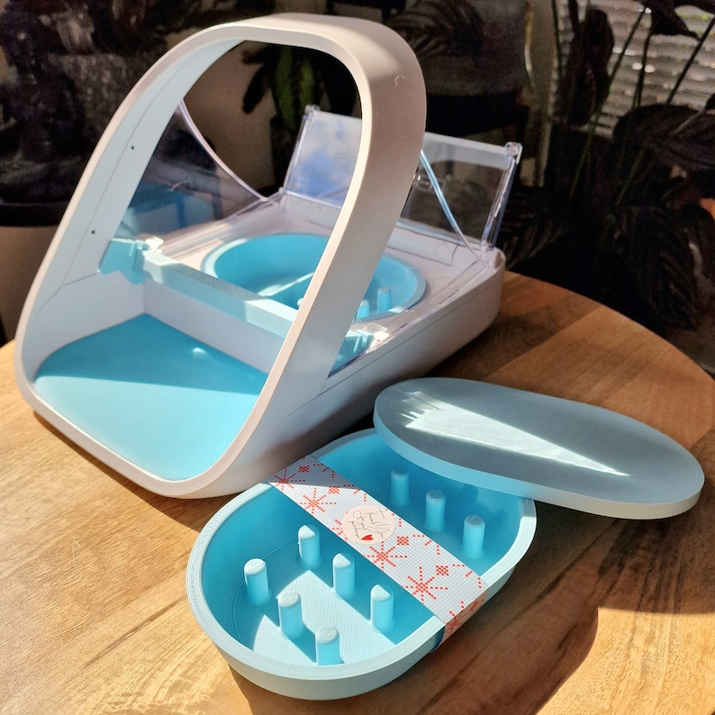 May include: A white and blue plastic device with a clear plastic lid. The device has a blue tray with a pattern of small holes. The device is designed for storing and organizing small items.