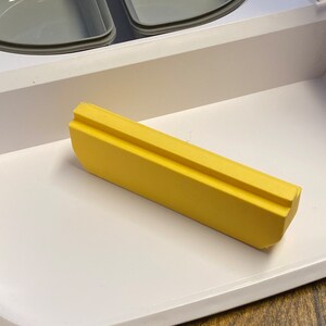 Peut inclure: Un insert de plateau en plastique jaune pour un petit appareil. L'insert a une forme rectangulaire avec une l&eacute;g&egrave;re courbe d'un c&ocirc;t&eacute;.