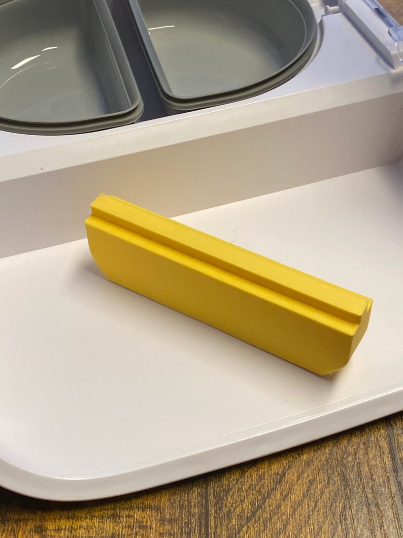 Peut inclure: Un insert de plateau en plastique jaune pour un petit appareil. L'insert a une forme rectangulaire avec une l&eacute;g&egrave;re courbe d'un c&ocirc;t&eacute;.