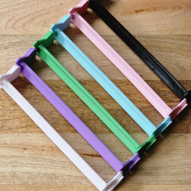 May include: Six plastic bag clips in different colors: white, purple, green, light blue, pink, and black. The clips are arranged in a row, with the white clip at the bottom and the black clip at the top.