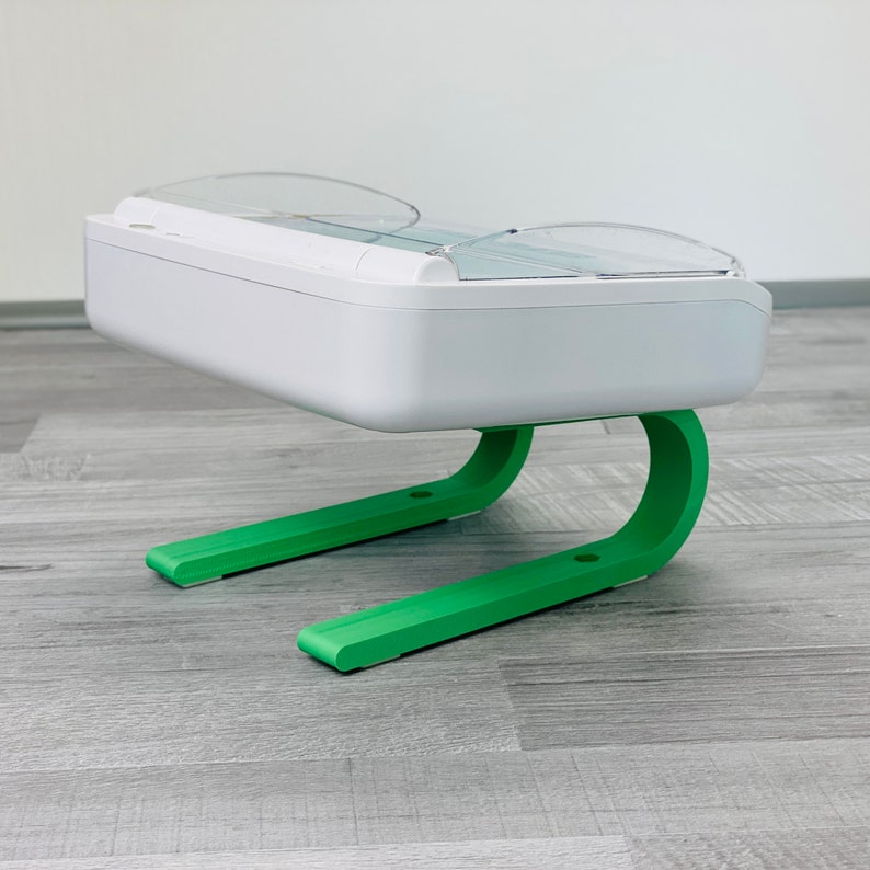 May include: A white pet feeder with a clear plastic top and green legs. The feeder has a rectangular base and a curved top.