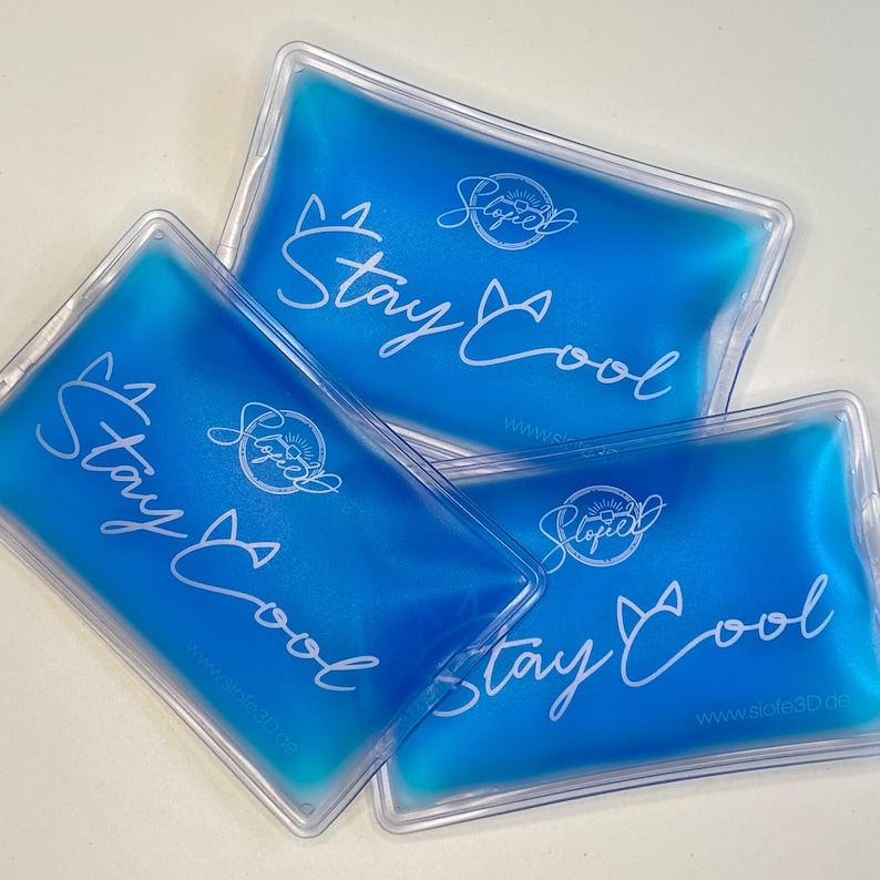 May include: Three rectangular, clear plastic ice packs filled with blue liquid. Each pack has the words "Stay Cool" in white script, along with a logo and website address. The packs are arranged on a white surface.
