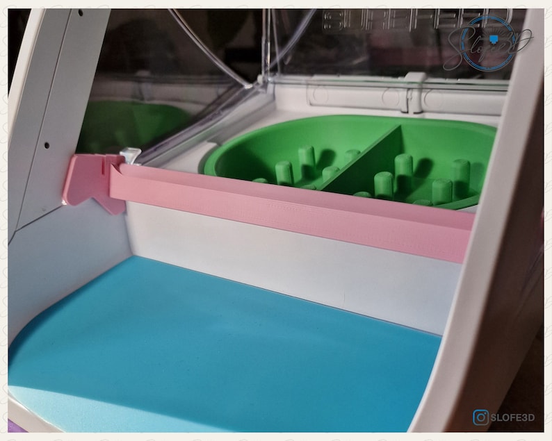 May include: A white pet feeder with a pink and blue tray. The feeder has a green maze-like bowl with two compartments.