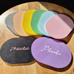 May include: A set of 10 colorful round coasters with the word "Phoebe" written on two of them. The coasters are made of a soft, spongy material and are perfect for protecting surfaces from scratches and spills.