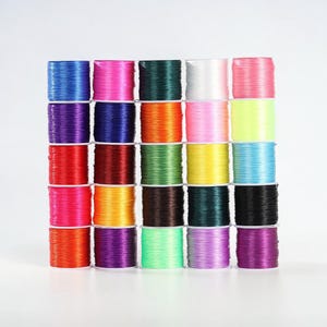 May include: A selection of vibrant elastic string spools in a range of colours, such as blue, pink, green, and yellow. The spools are arranged in a neat stack, creating a visually pleasing arrangement. Suitable for crafts and jewellery making.