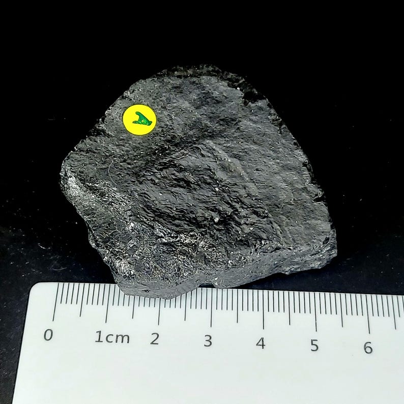 Natural black tourmaline rough stone photographed on black background with ruler for scale
