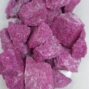 Op de afbeelding: Een stapel ruwe, magenta-gekleurde mineraalmonsters. De rotsen hebben een kristallijne structuur en een licht poreuze textuur. De kleur is consistent, met sommige gebieden die een lichtere, bijna witte tint vertonen.