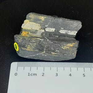 Unpolished black tourmaline stone photographed horizontally with ruler for size