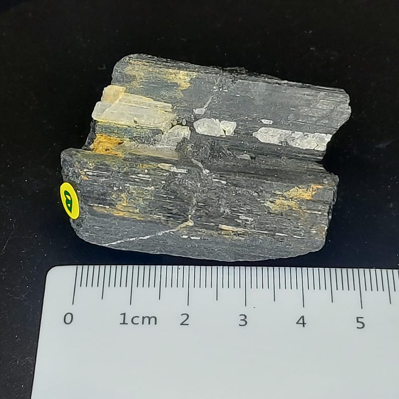 Unpolished black tourmaline stone photographed horizontally with ruler for size