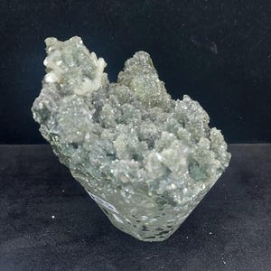 Angled view of green chalcedony druzy crystal cluster on black background