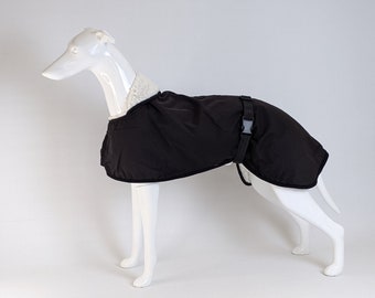 May include: A black dog coat featuring a white faux-shearling collar and a black adjustable strap with a plastic buckle closure. The coat is displayed on a white mannequin shaped like a greyhound, covering the torso and back area of the figure.