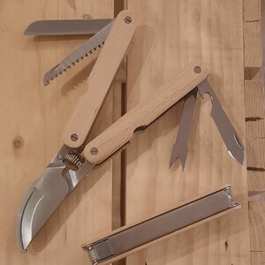 Peut inclure: Un ensemble d'outils de jardinage multifonctionnels avec des manches en bois et diverses lames en acier inoxydable, dont un sécateur, une scie et un couteau. L'ensemble comprend également un petit étui de rangement rectangulaire.