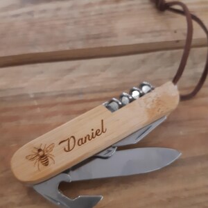 Peut inclure: Un couteau de poche en bois avec une abeille et le nom "Daniel" gravé sur le manche. Le couteau possède un tire-bouchon, un ouvre-bouteille et une petite lame.