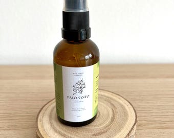 Puede incluir: Una botella de vidrio marrón con una boquilla de pulverización negra y una etiqueta blanca. La etiqueta dice "Wild Forest Candles Palo Santo Air Spray Made from 100% natural ingredients 50ml". La botella está sentada sobre una rodaja redonda de madera.