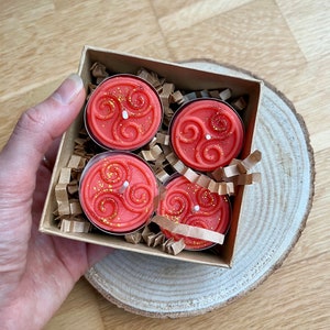 May include: Four orange tea light candles with a gold swirl design in a brown box with shredded paper.