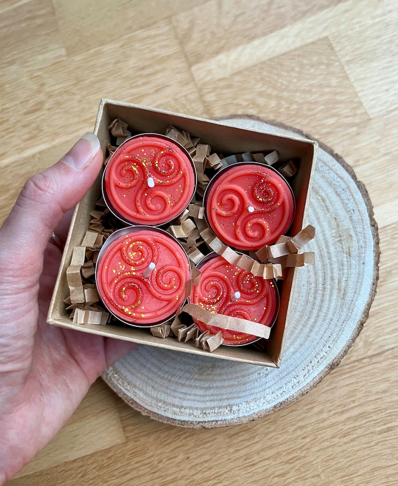 May include: Four orange tea light candles with a gold swirl design in a brown box with shredded paper.