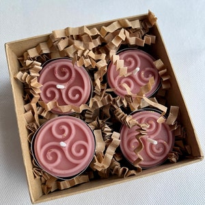May include: Four pink tea light candles with a gold triquetra design in a brown cardboard box with shredded paper packing.