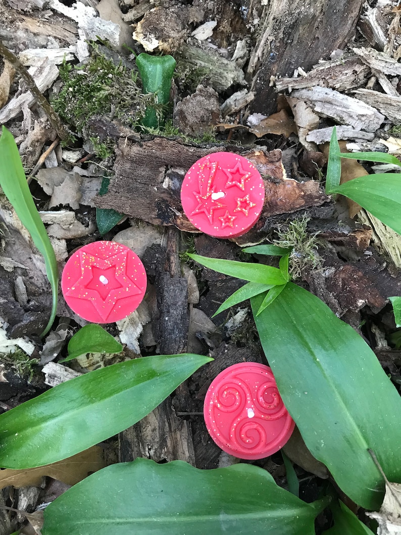 Op de afbeelding: Drie rode wax melts met verschillende ontwerpen. De eerste kaars heeft een stervormig ontwerp, de tweede kaars heeft een swirl-ontwerp en de derde kaars heeft een stervormig ontwerp met glitter.