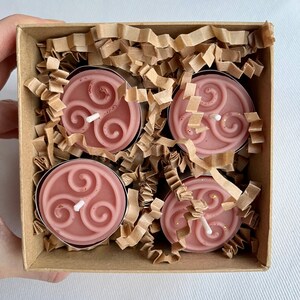 May include: Four pink tea light candles with a white triquetra design in a brown box with shredded paper.