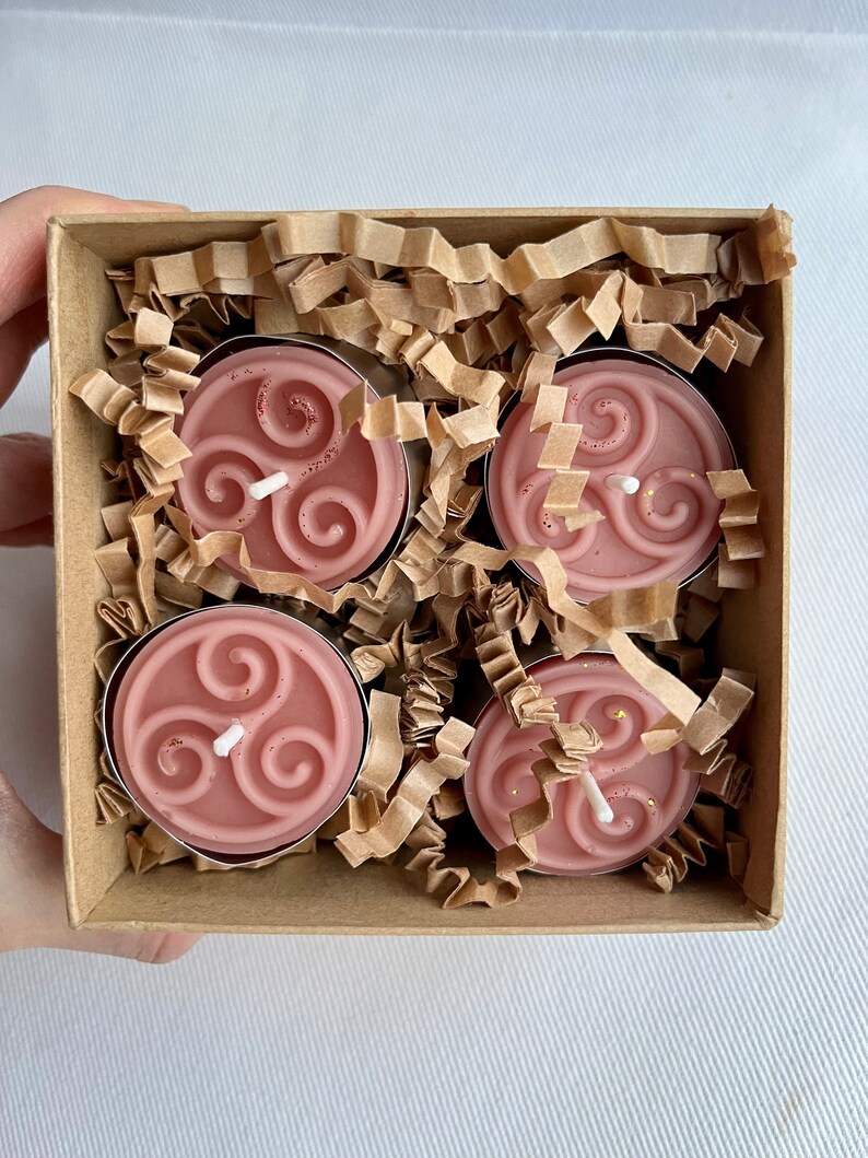 May include: Four pink tea light candles with a white triquetra design in a brown box with shredded paper.
