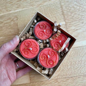 May include: Four red tea light candles with a gold swirl design in a brown box with shredded paper.