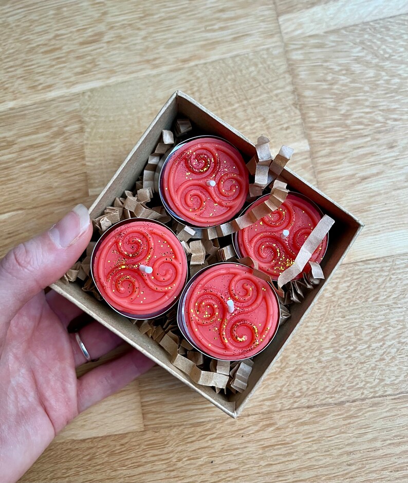 May include: Four red tea light candles with a gold swirl design in a brown box with shredded paper.