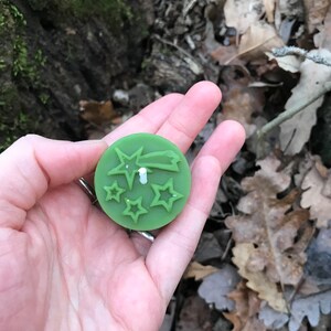 Op de afbeelding: Een groene kaars met een ster- en vallende ster-ontwerp. De kaars wordt in de hand van een persoon gehouden.