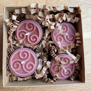 May include: Four pink tea light candles with a Celtic knot design in a brown cardboard box with shredded paper.