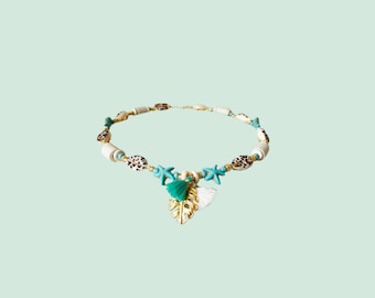 May include: A white and gold necklace with turquoise and brown accents. The necklace features a gold leaf charm with a white and turquoise tassel.