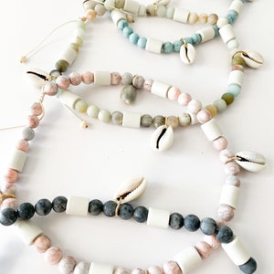 May include: A set of five bracelets featuring different colored stones and white beads. Each bracelet has a small seashell charm.